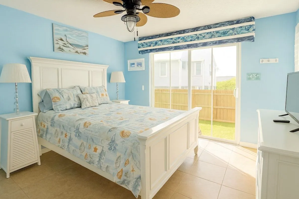 Second bedroom with a queen bed, sky-blue walls, coastal bedding, smart TV and sliding doors to the back patio
